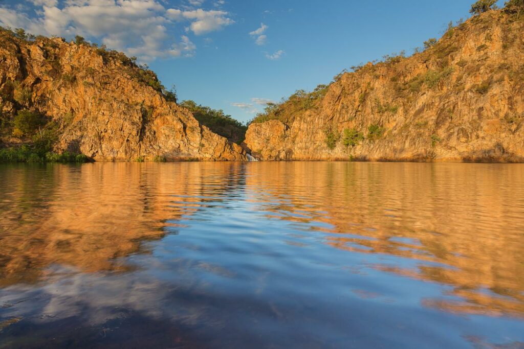 greenery covered outcrop in Northern Territory with blue skies and water reflection
