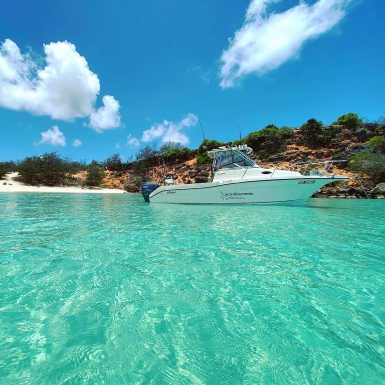 power fishing boat floating on crystal clear waters by an island with blue skies and a few clouds fishing rods off the side of the boat
