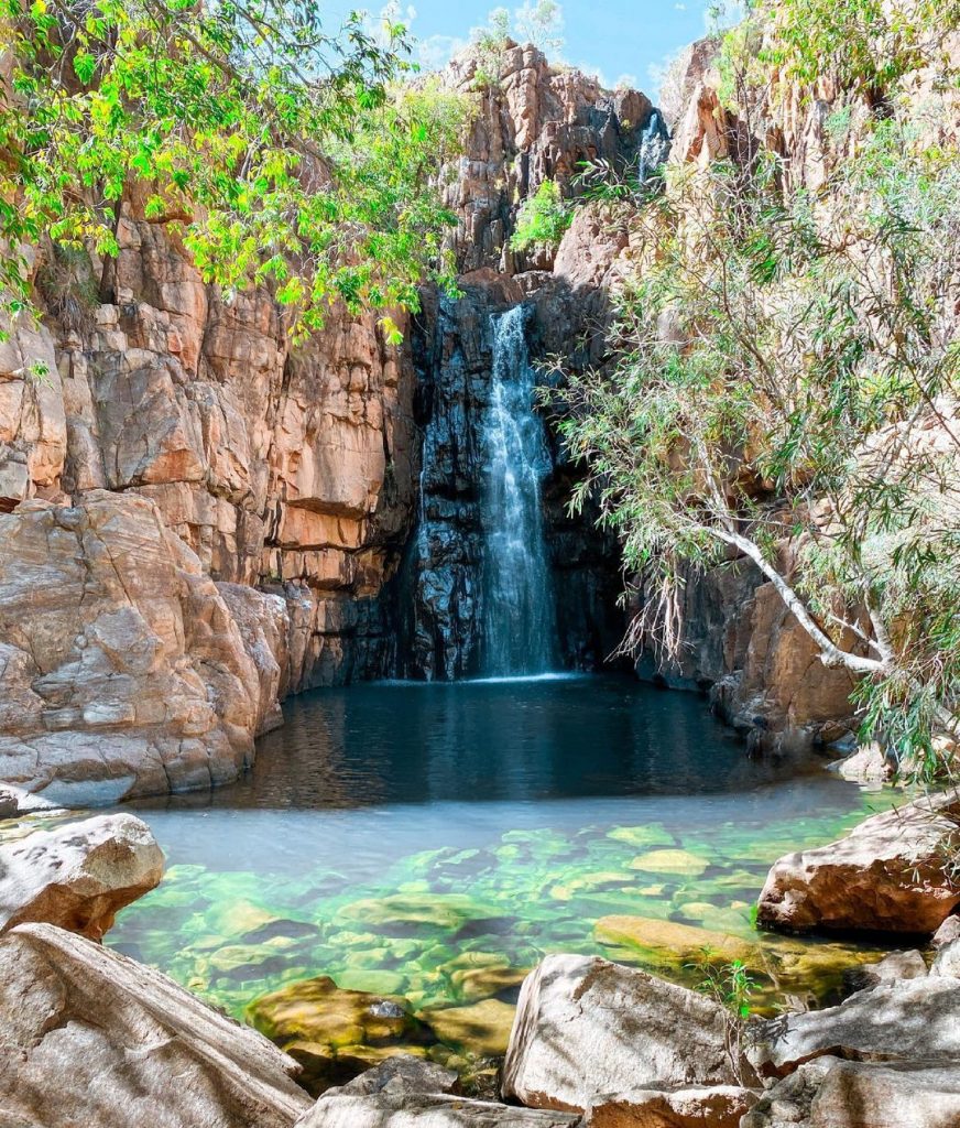 Waterfall cascading into clear blue water pools with red rock surrounds in the Northern Territory Australi