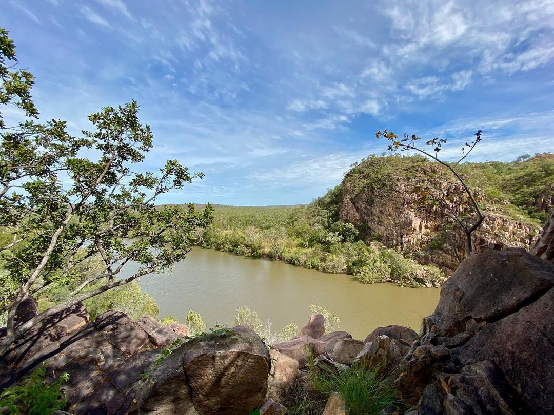 a murky river in between green grass and rock structures with sparse trees surrounding the river and blue skies on the Jatbula Trail
