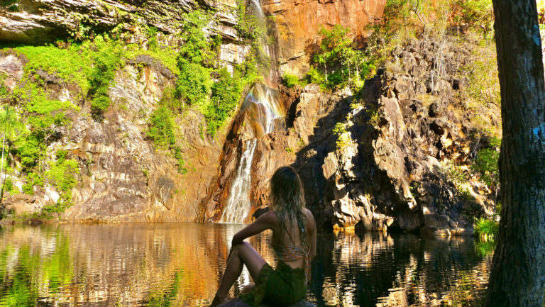 woman sitting at edge of water overlooking waterfall