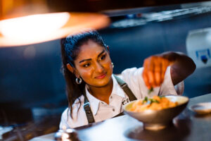 woman sprinkling seasoning on a dish