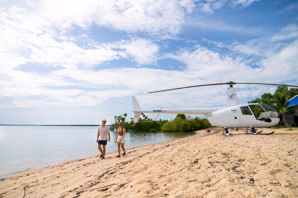 two people walking across the sand with helicopter in backdrop