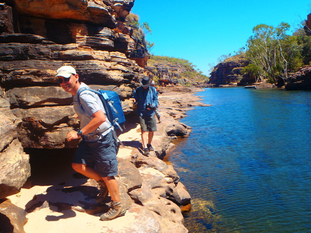 two men walking on the edges of a body of water with blue skies