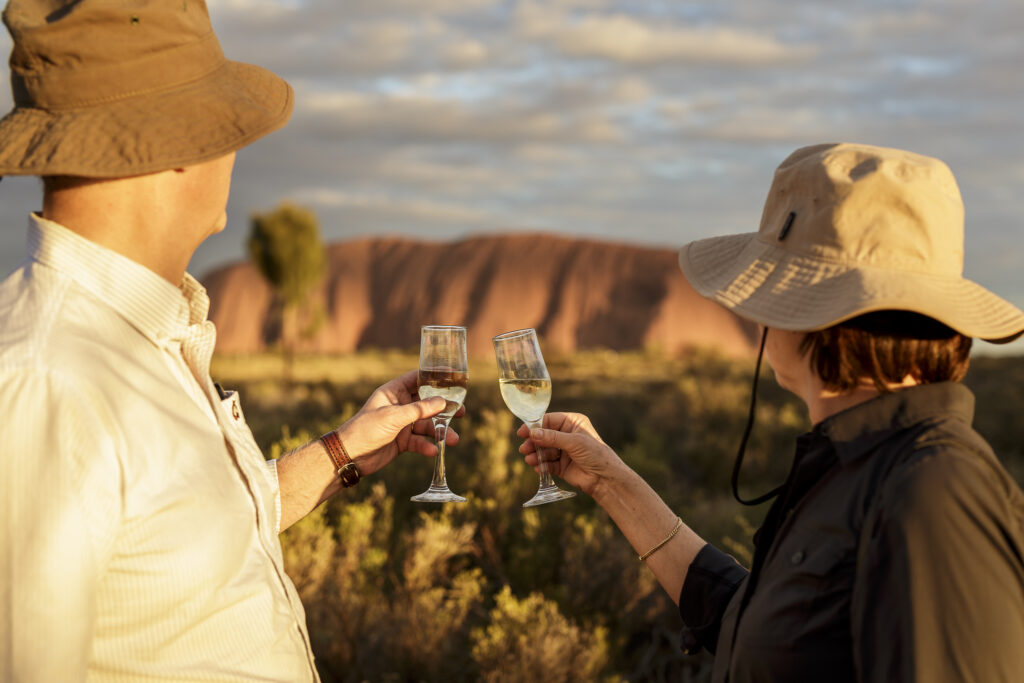 two people cheering with champagne with Uluru in backdrop